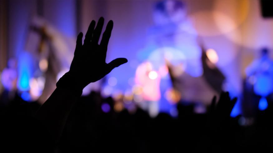 Fotografia de várias mãos numa Igreja à noite erguidas para os céus