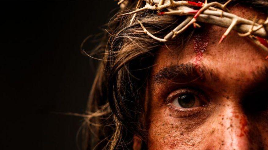 Fotografia dos olhos de Jesus, rodeado por sardas, uma coroa de gravetos e sangue escorrendo da testa