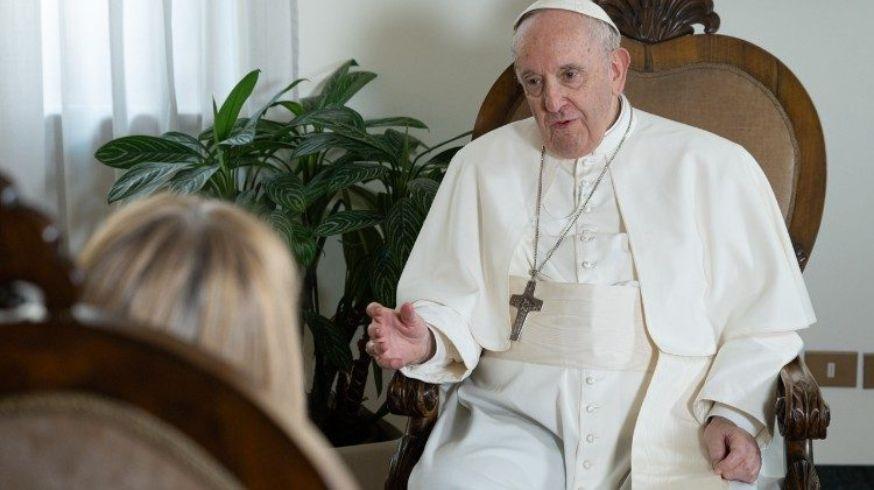 Fotografia do Papa Francisco sentado, dialogando com uma mulher que está de costas para a câmera